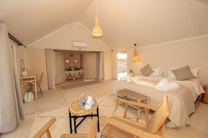 Une chambre spacieuse aménagée comme une tente, avec un lit, un coin salon et une salle de bain.