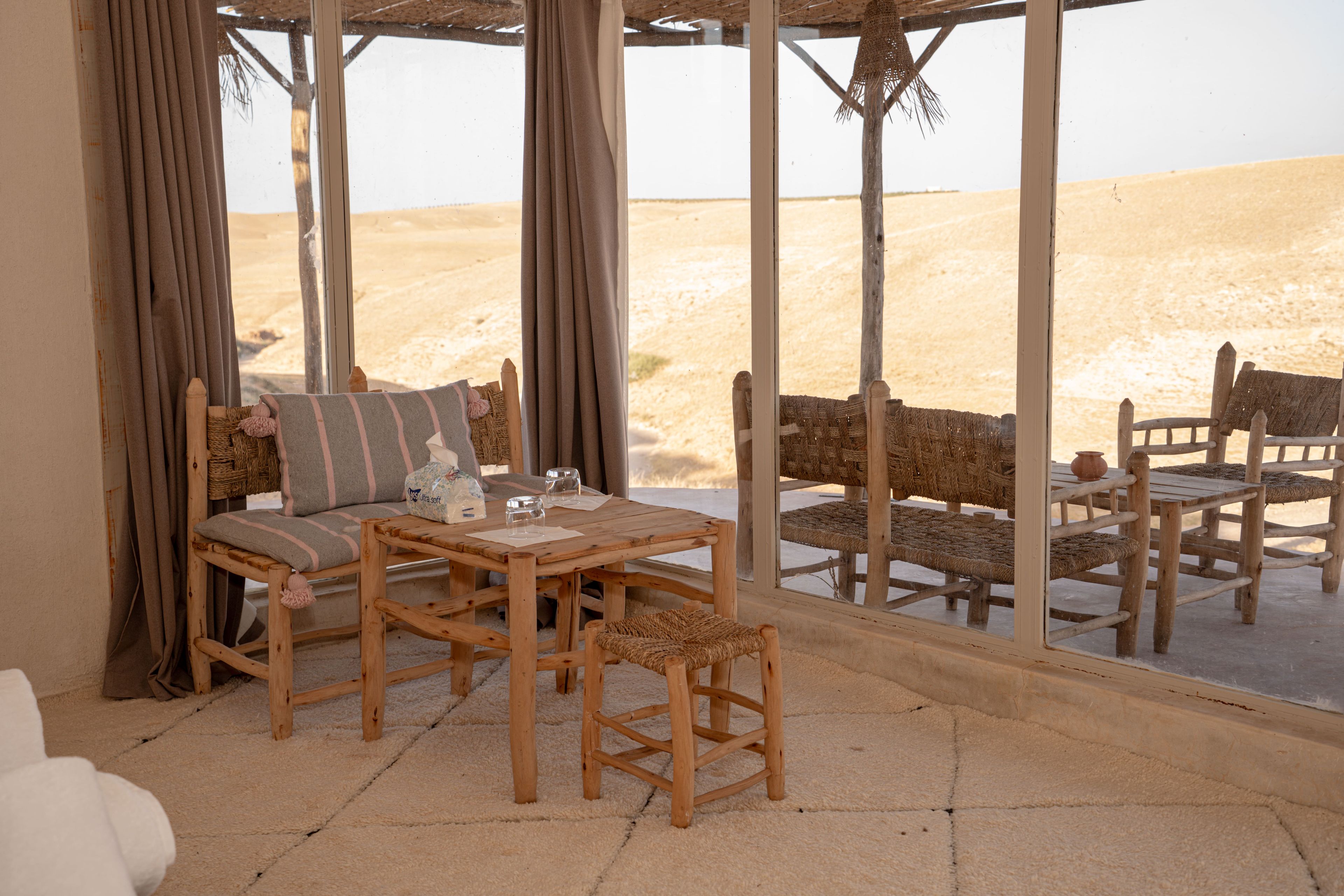 A room with a wooden table and chairs, a sofa, and a view of the desert through large windows.