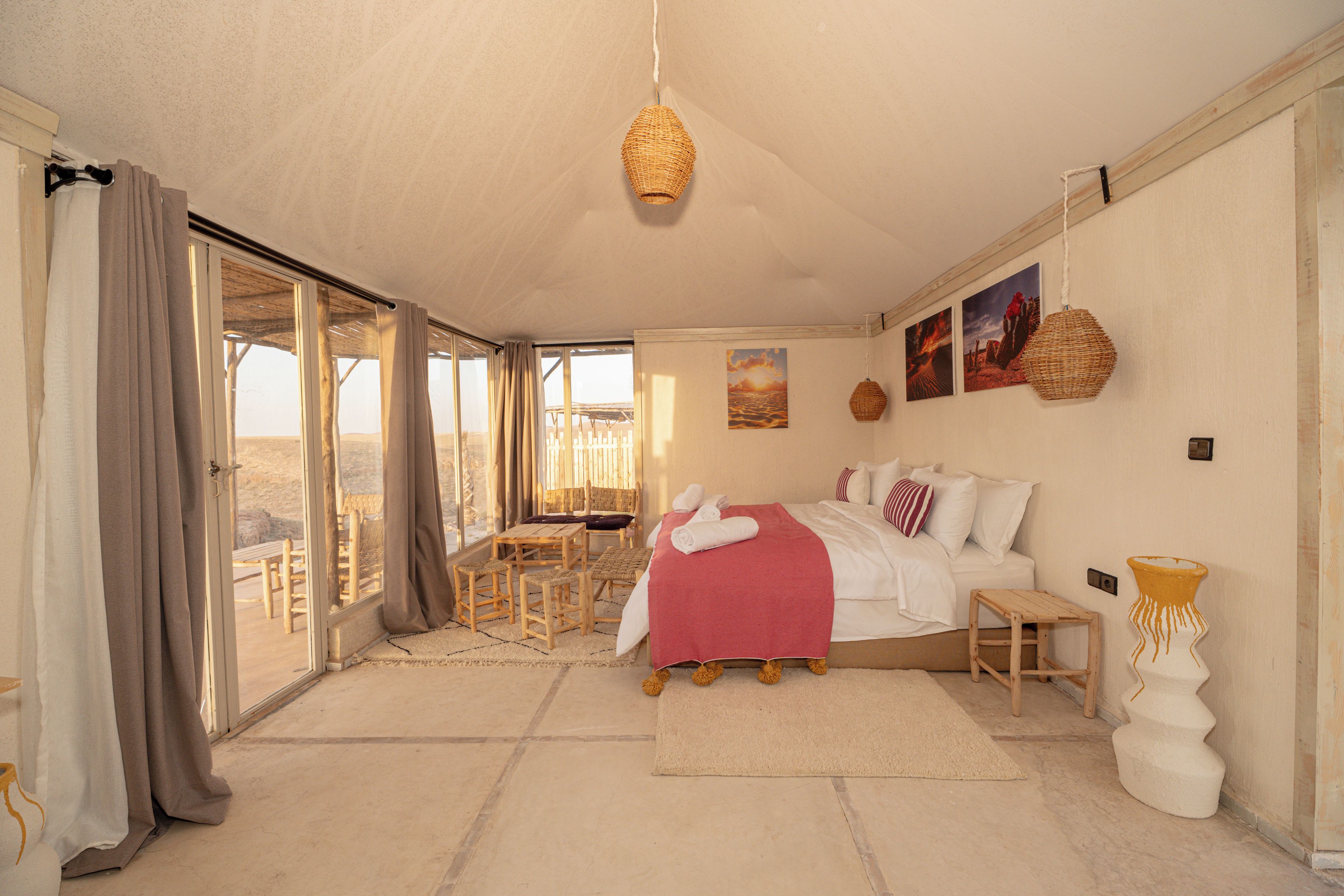 Une chambre spacieuse avec un grand lit, une petite table et une chaise. Elle dispose d’un balcon avec vue sur le désert.