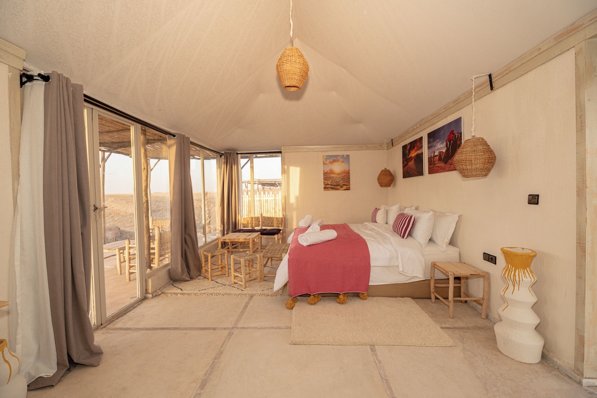 Une chambre spacieuse avec un grand lit, une petite table et une chaise. Elle dispose d’un balcon avec vue sur le désert.