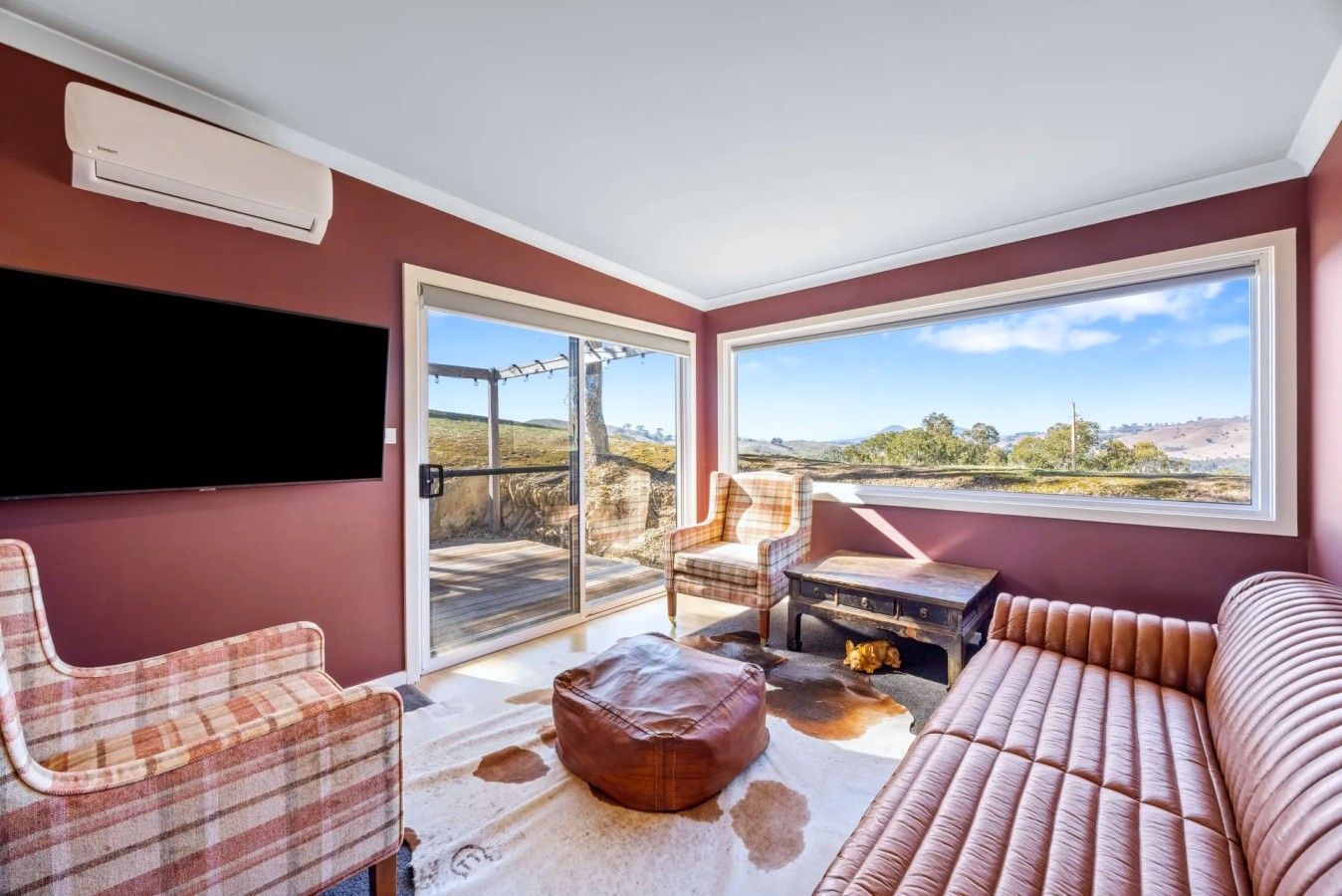 A room with a large window, a flat-screen TV, a plaid chair, a leather sofa, and a wooden coffee table.
