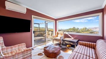 A room with a large window, a flat-screen TV, a plaid chair, a leather sofa, and a wooden coffee table.