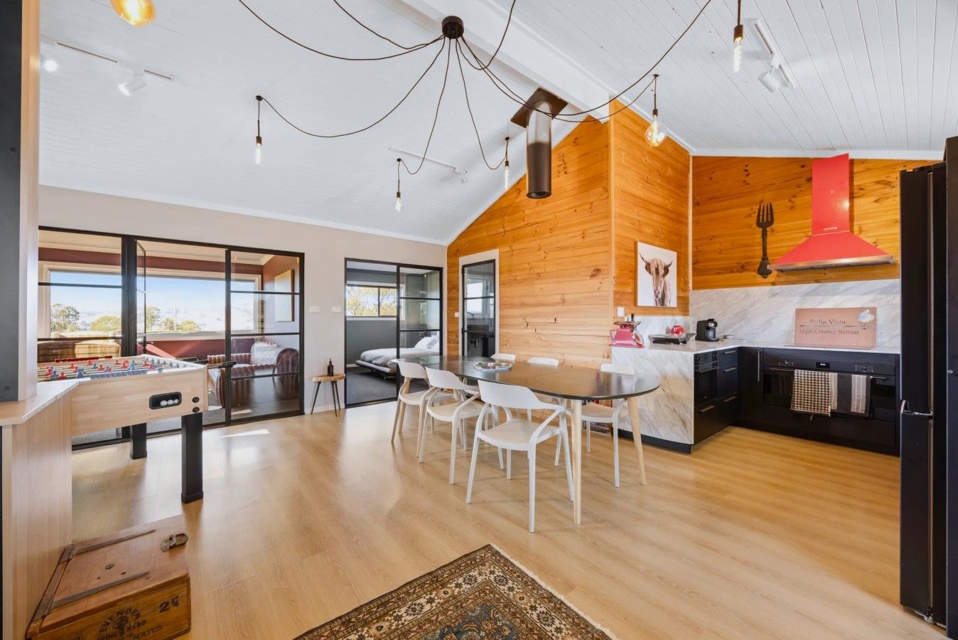 Un interior moderno con comedor, cocina y vistas amplias a través de grandes ventanas.
