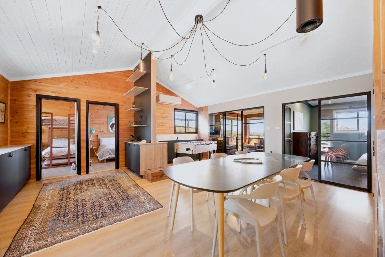 A modern interior with a dining area, kitchen, and a bedroom with bunk beds.