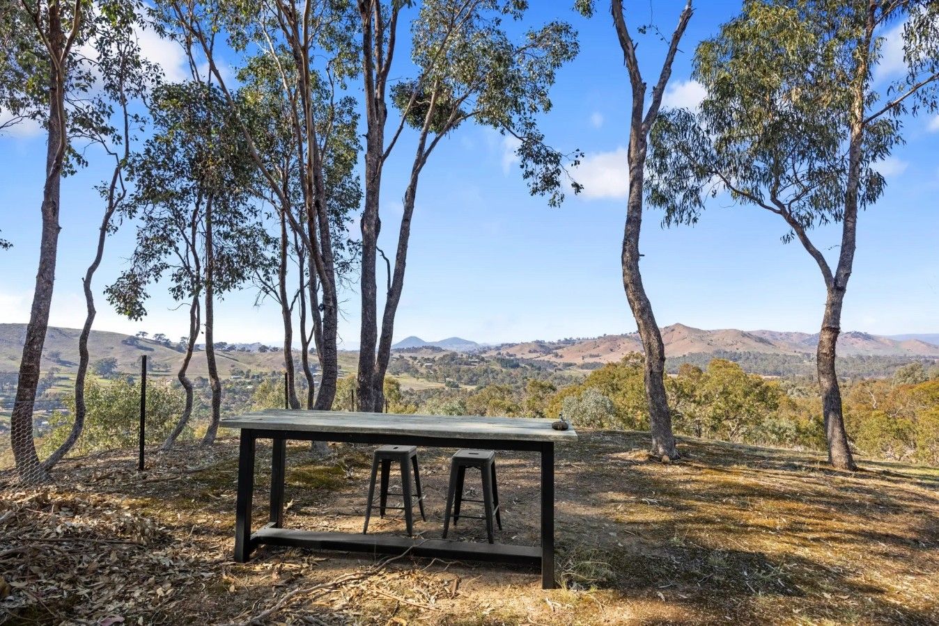 A picnic table with stools in a natural setting with trees and a view of distant hills.