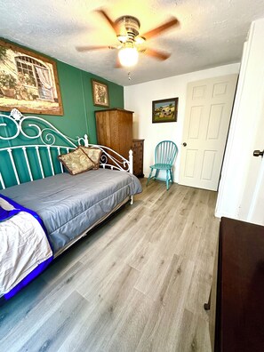 Ein Schlafzimmer mit einem Bett, einem Holzschrank, einem blauen Stuhl und einem Deckenventilator.