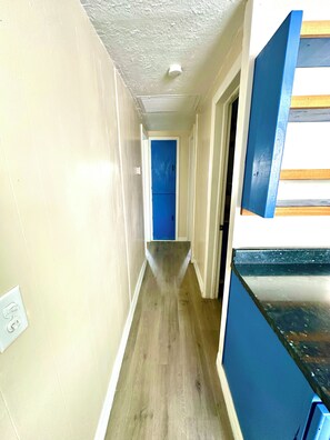 Ein schmaler Gang mit Holzboden, einer blauen Tür am Ende und einer weißen Decke mit einer Leuchte.