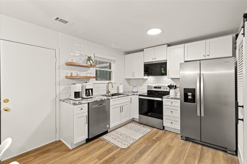 Una cocina moderna con armarios blancos, electrodomésticos de acero inoxidable y piso de madera.