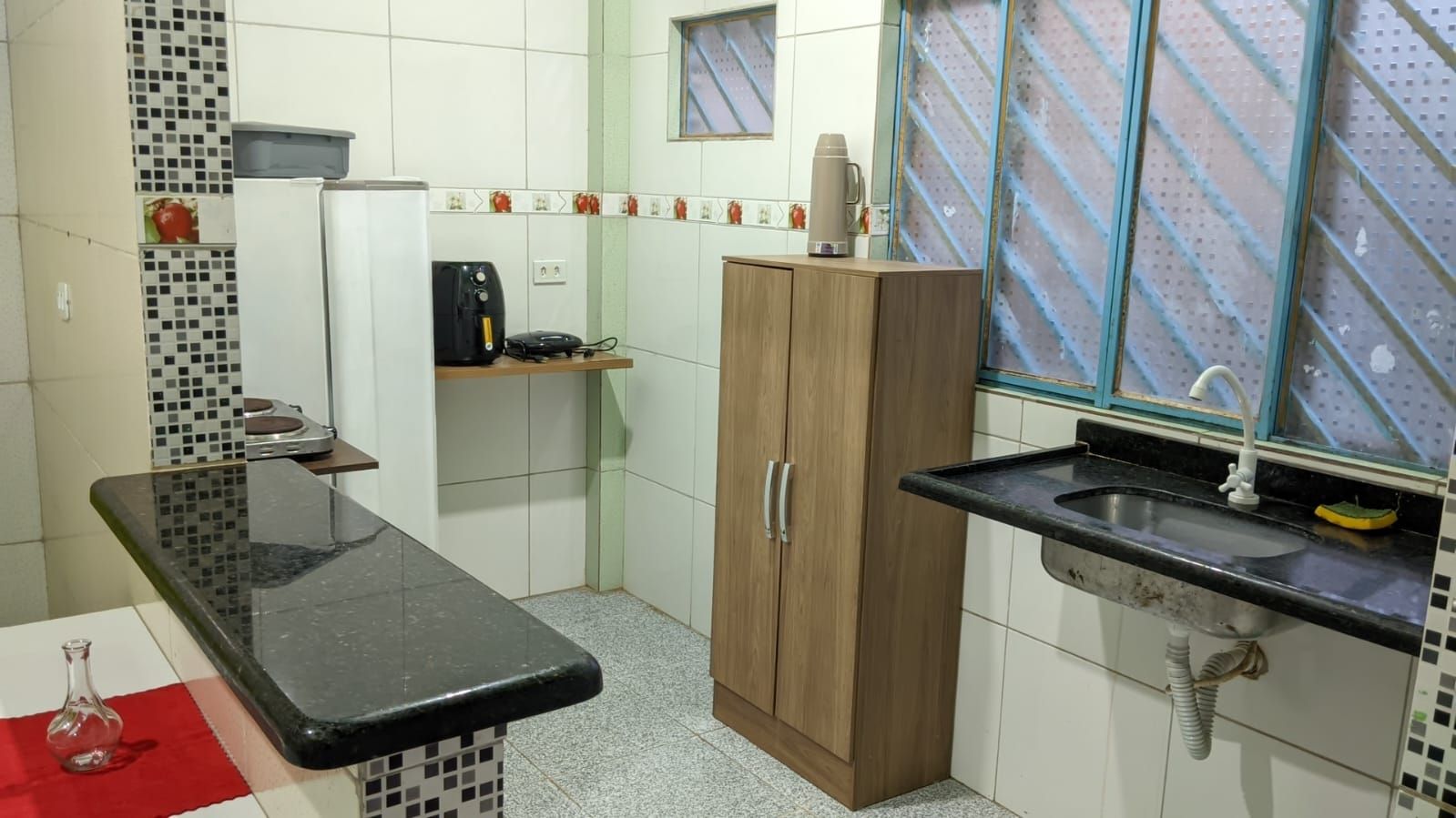 Cozinha com bancada preta, armário de madeira, pia e micro-ondas.
