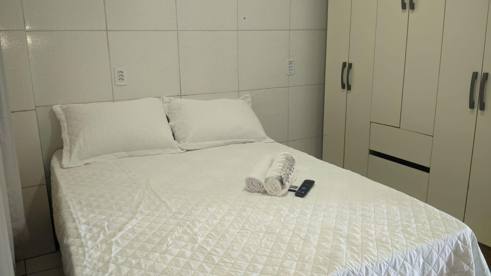 Quarto de hotel com cama, um conjunto de toalhas e controle remoto.