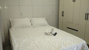 A neatly made bed with a quilted cover, two pillows, a rolled towel, and a remote control on the bed.