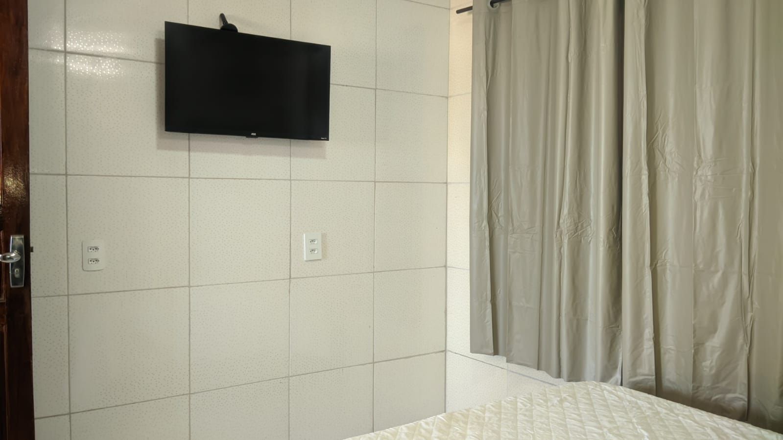 Quarto com uma cama, televisão na parede e cortina de chuveiro.