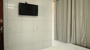 Een kamer met een bed, een aan de muur bevestigde televisie en een douchegordijn.