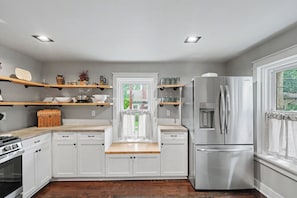 A modern kitchen with white cabinets, stainless steel appliances, and wooden countertops.