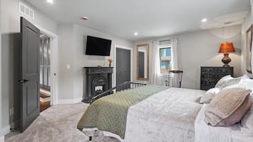 A bedroom with a bed, a fireplace, a television, and a window with curtains.