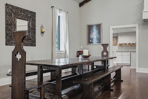 A dining area with a wooden table and benches, a decorative mirror, a wall-mounted light, and a window with curtains.