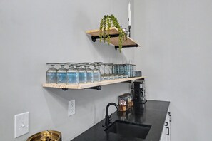 Una cocina con un lavamanos negro, una repisa de madera con frascos de vidrio y una planta colgante.