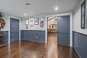 Un pasillo con piso de madera, una serie de cuadros enmarcados en la pared y una puerta que da a una habitación con sofá.