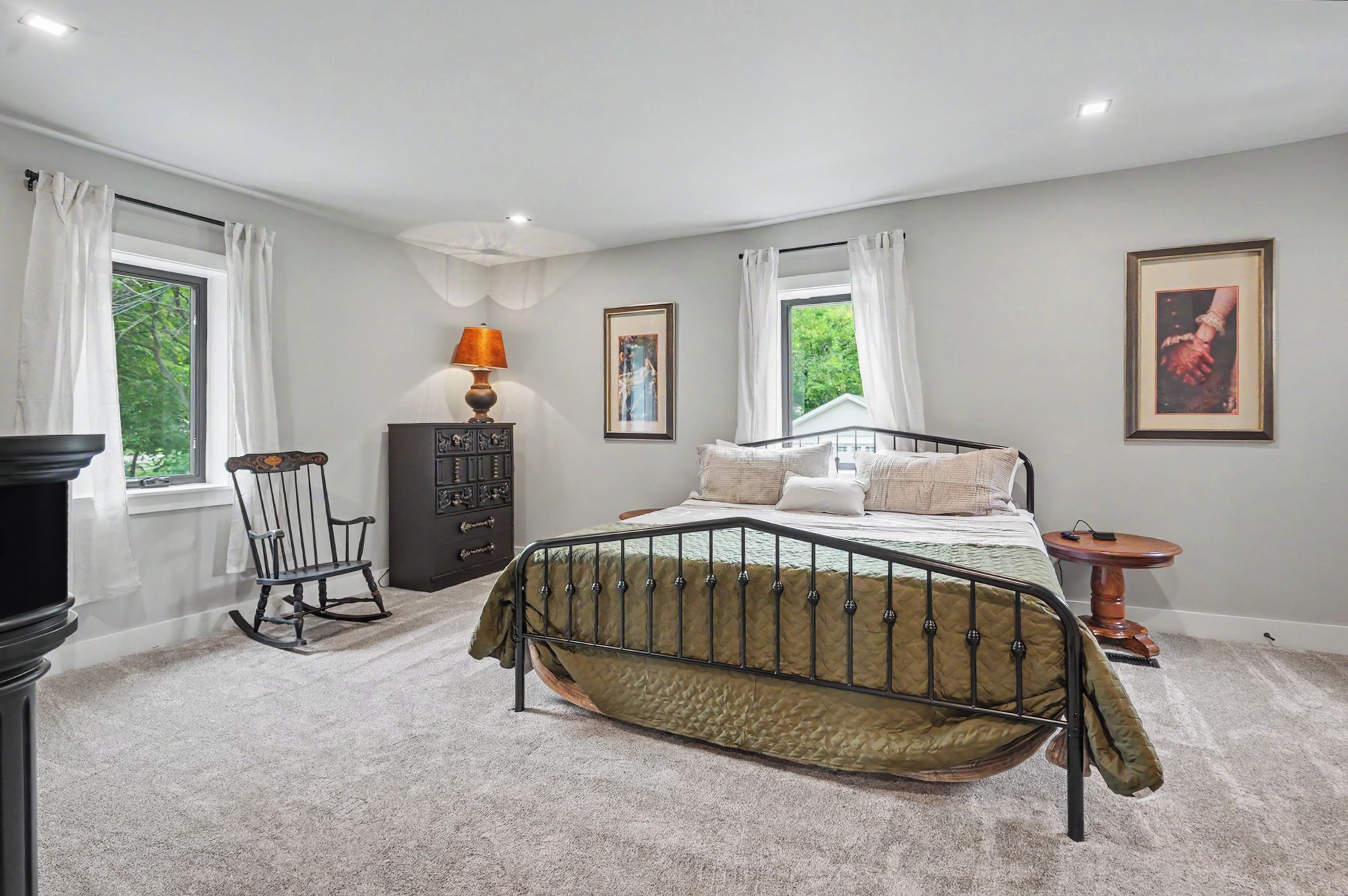 A bedroom with a bed, dresser, chair, lamp, and artwork.