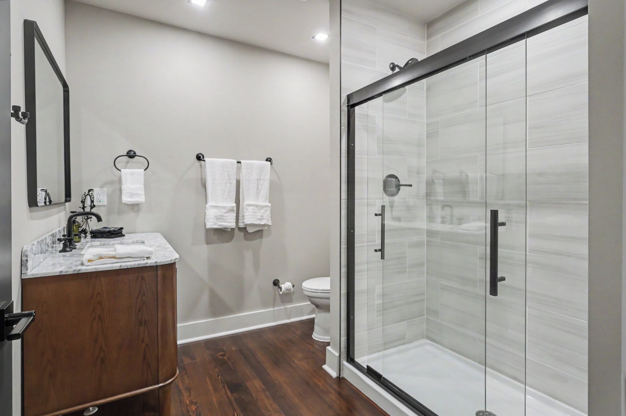 A modern bathroom with a glass-enclosed shower, a wooden vanity, and a white toilet.