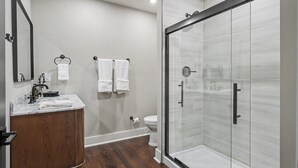 Un baño moderno con ducha de vidrio, tocador de madera y inodoro blanco.