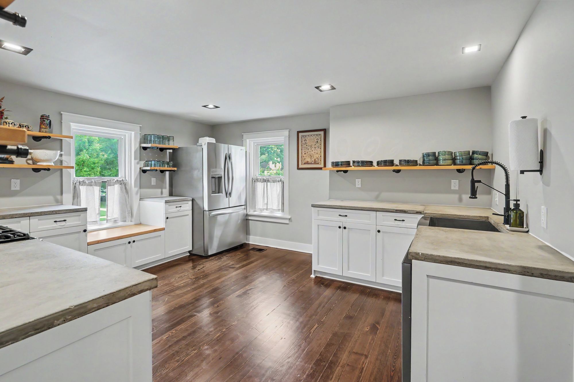 A modern kitchen with white cabinetry, a stainless steel refrigerator, wooden countertops, and a view of greenery outside.