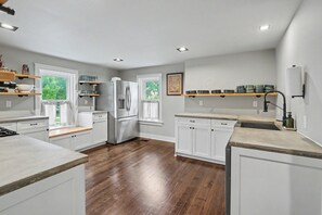 Cocina moderna con armarios blancos, refrigerador de acero inoxidable, encimeras de madera y vistas al exterior.