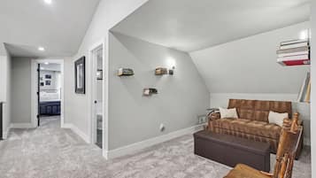 A bedroom with a sloped ceiling, a brown sofa, a wooden chair, and a bookshelf.