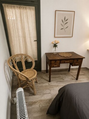 A room with a wicker chair, a wooden table with a vase of flowers, a framed botanical print on the wall, and a radiator. - Guest apartment in an unbeatable location in Palermo (Buenos Aires)