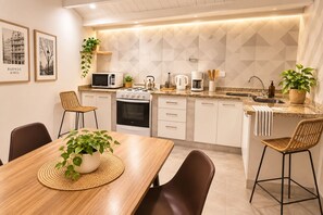 A modern kitchen with white cabinets, a microwave, stove, and sink. There are two wicker chairs and a dining table with a plant. - Guest apartment in an unbeatable location in Palermo (Buenos Aires)