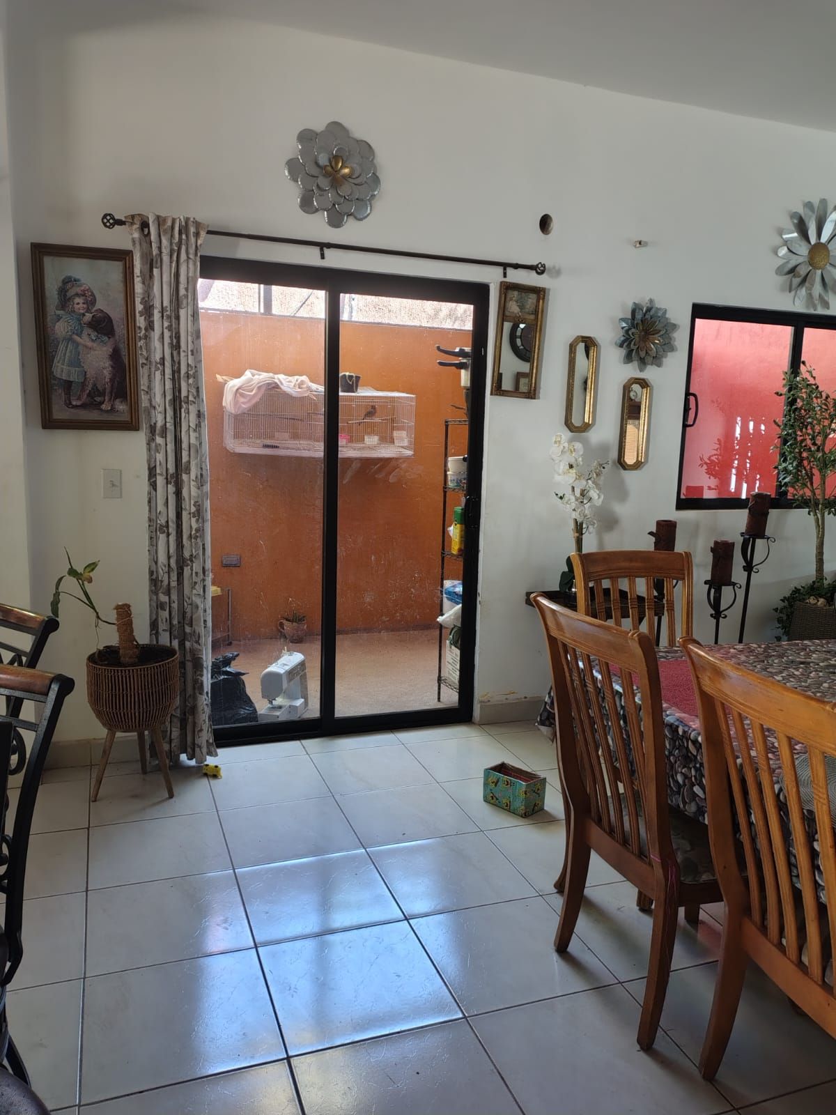 Comedor con mesa y sillas, puerta corredera de vidrio que da a un espacio exterior y diversas decoraciones en la pared.