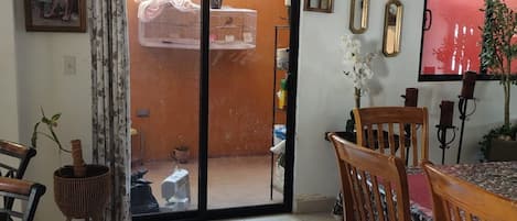 Comedor con mesa y sillas, puerta corredera de vidrio que da a un espacio exterior y diversas decoraciones en la pared.
