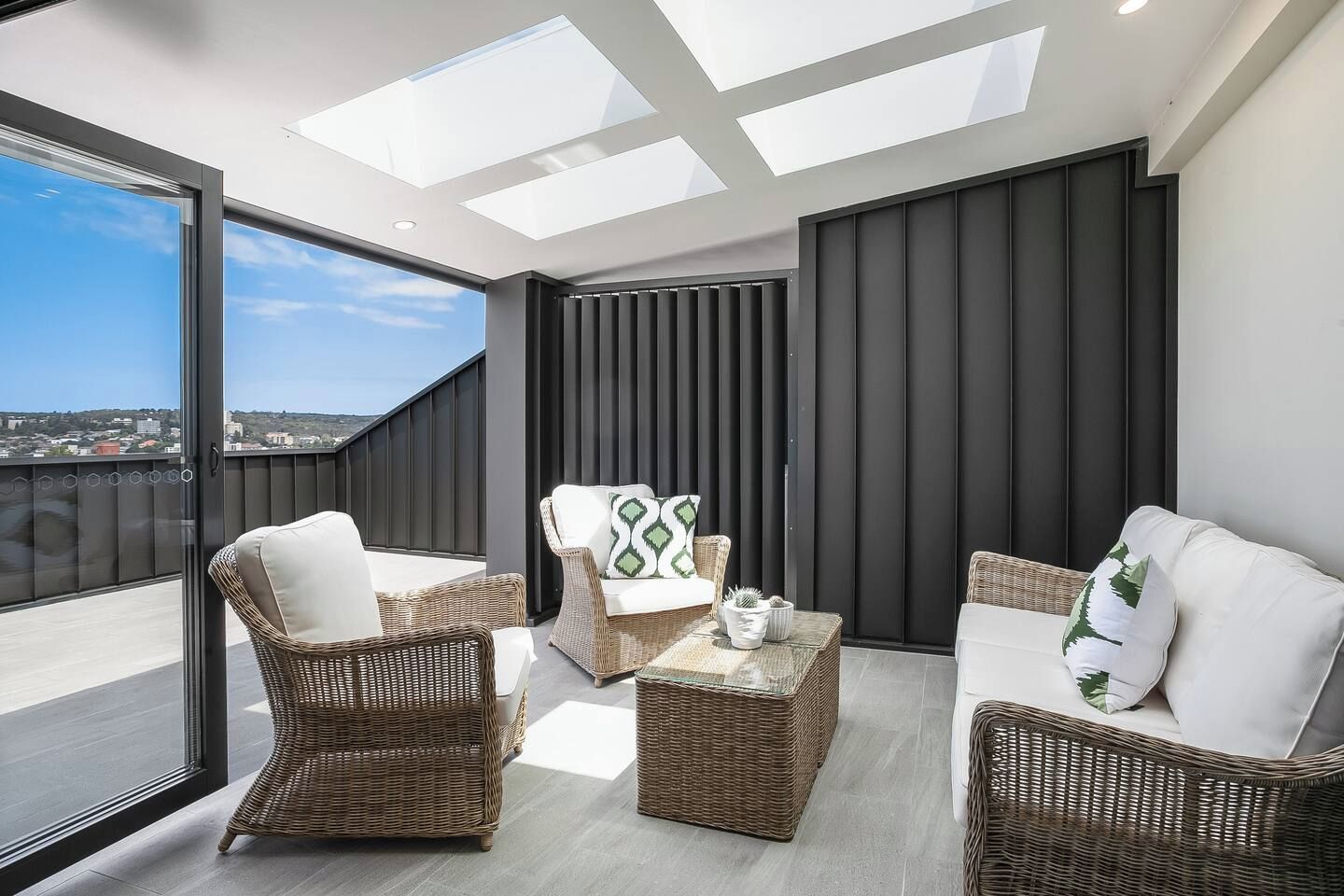 A modern balcony with wicker furniture, a glass door, and a view of the city.