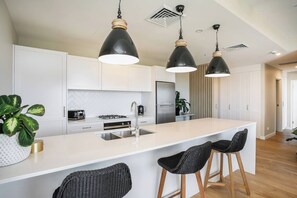 Eine moderne Küche mit weißen Schränken, einer zentralen Kochinsel mit Barhocker und Pendelleuchten.