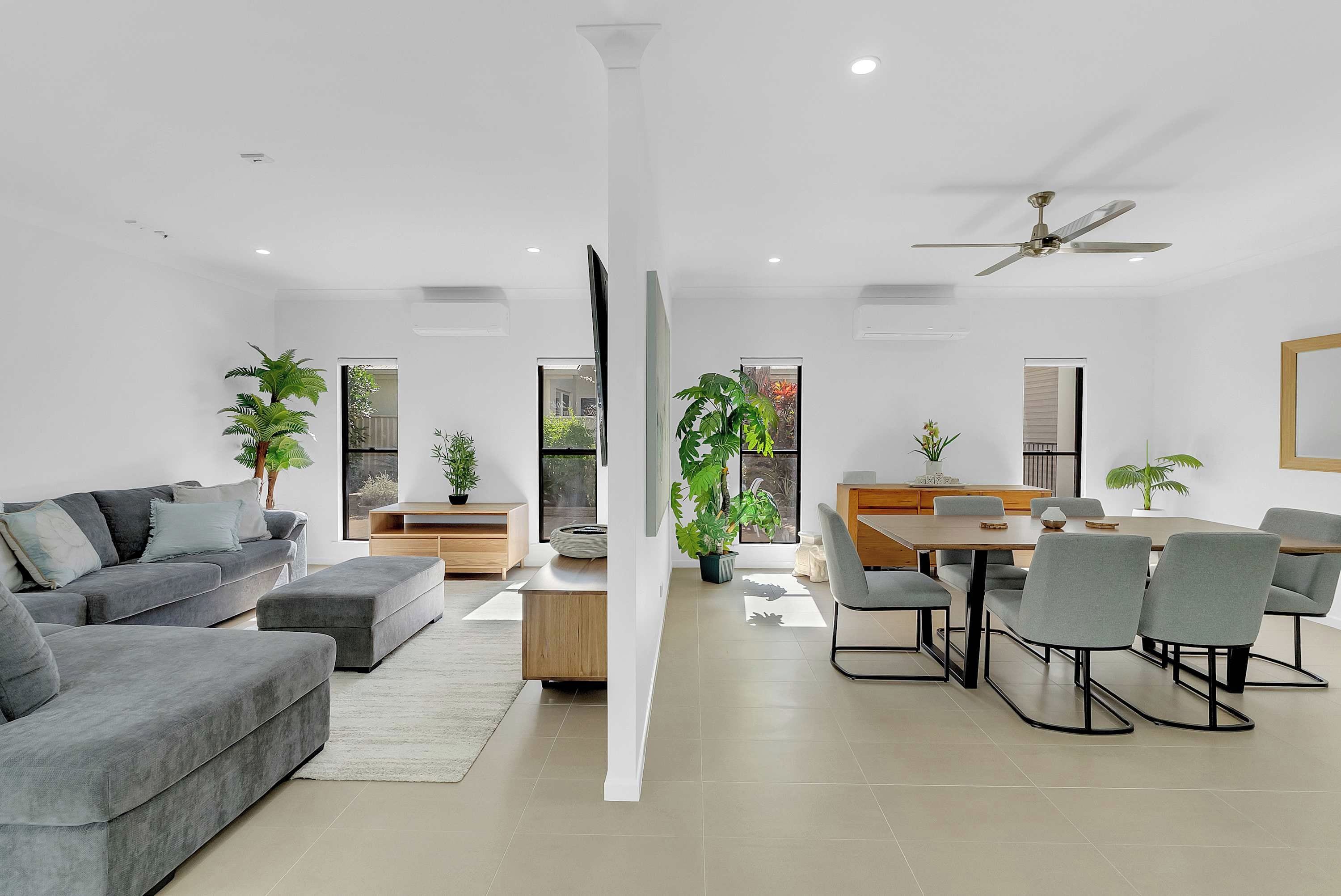 A modern living space with a grey sofa, a dining table with chairs, and potted plants.