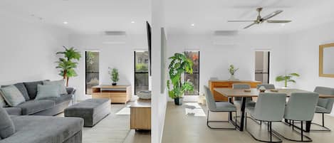 A modern living space with a grey sofa, a dining table with chairs, and potted plants.