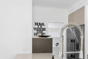A modern kitchen with a stainless steel refrigerator, a black countertop, and a wall-mounted light fixture. - Cedar Cove - Tropical Escape near Palm Cove Beach (Palm Cove)
