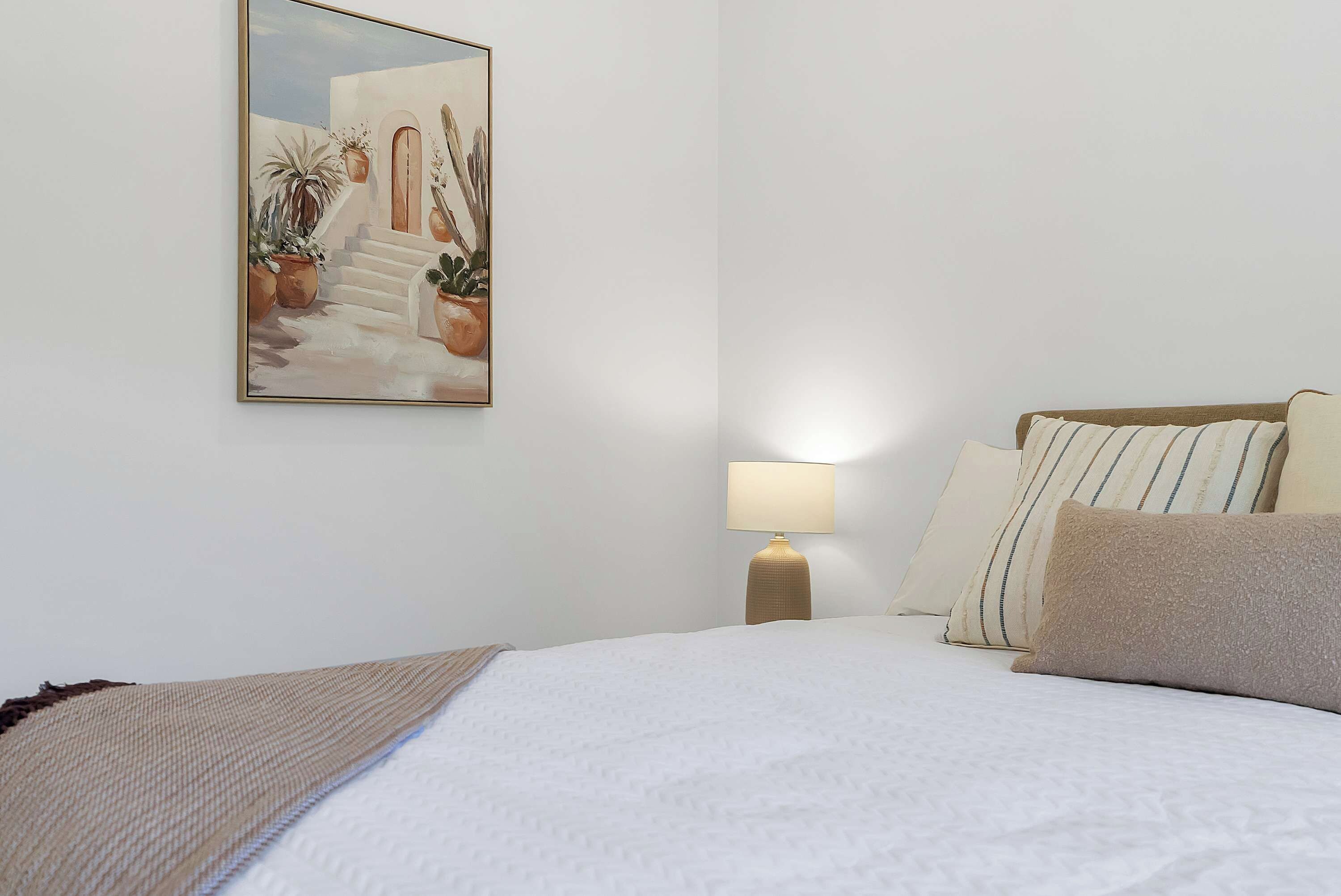 Quarto de hotel com cama, almofadas, luminária e um quadro na parede.