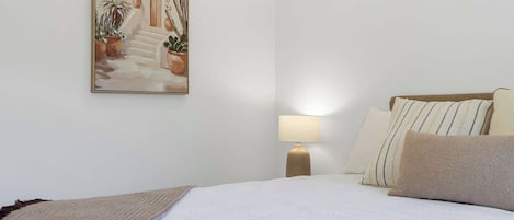 Quarto de hotel com cama, almofadas, luminária e um quadro na parede.