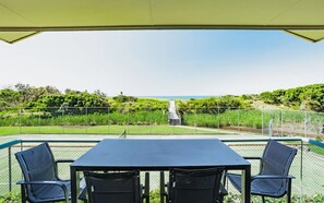 Een terras met een tafel en stoelen, met uitzicht op een kustlandschap met een pad dat naar de zee leidt.
