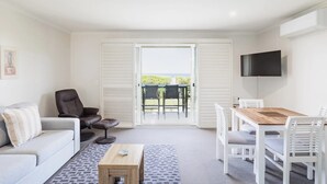 En stue med sofa, sofabord, fjernsyn ophængt på væggen samt spiseområde med stole og bord.