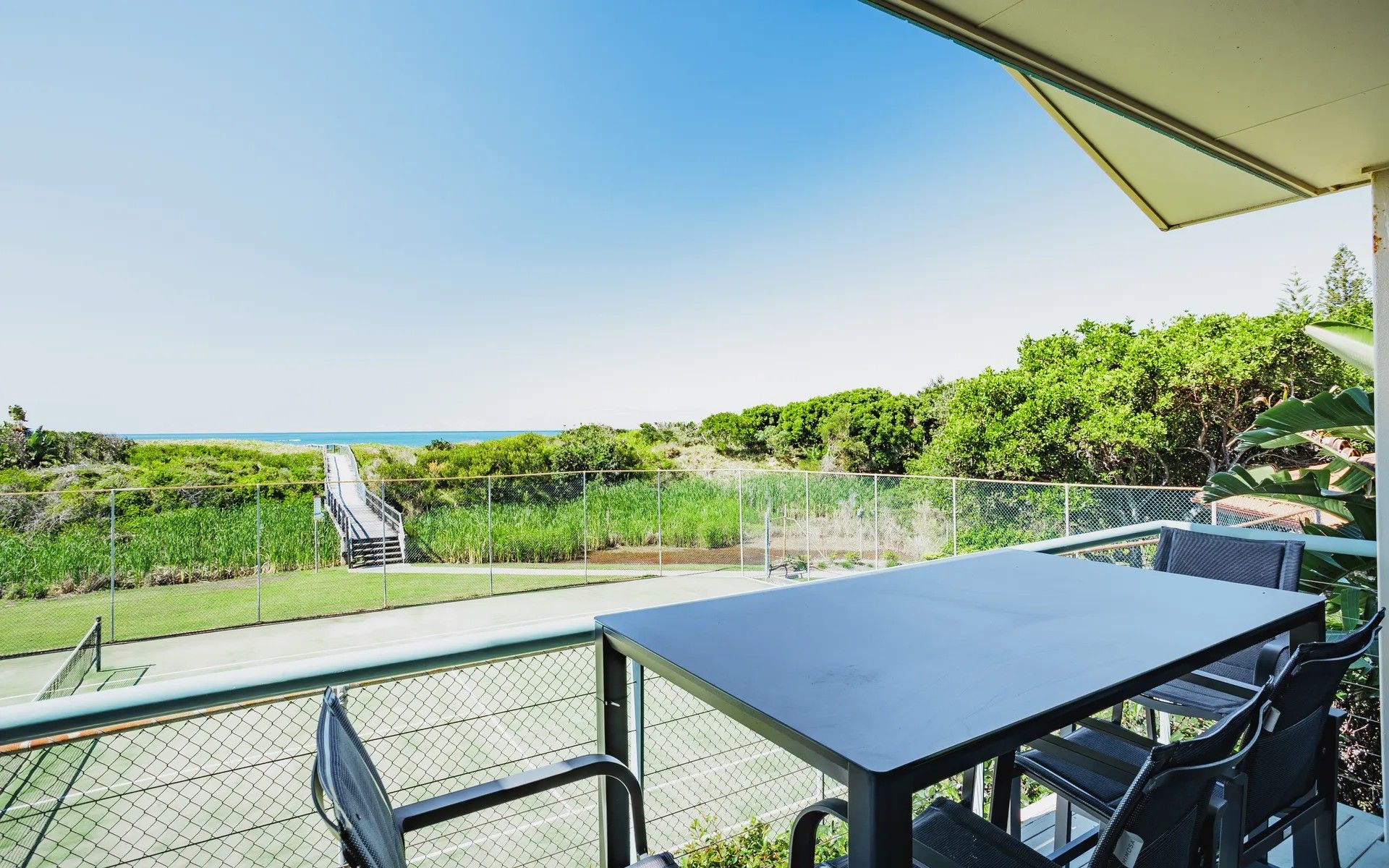 Un balcon avec vue sur la plage, une table et des chaises.