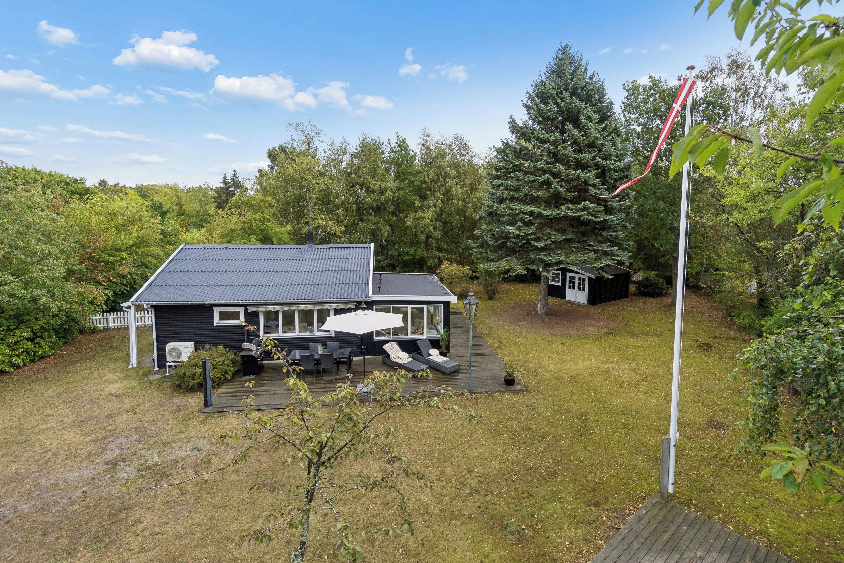 Une maison avec une terrasse, un espace barbecue et un petit abri de jardin.