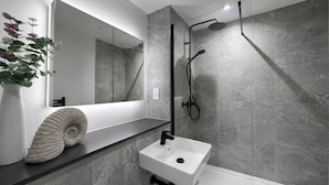 A modern bathroom with a glass shower enclosure, a white sink, and a marble-tiled wall. - Downtown Manchester Townhouse w/ Garden & Modern (Greater Manchester)