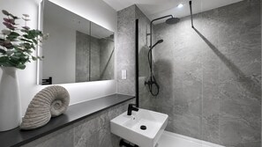 Un baño moderno con cabina de ducha de vidrio, un lavabo blanco y pared revestida de mármol.