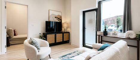 A modern living room with a sofa set, a television, and a window with a view of the street.