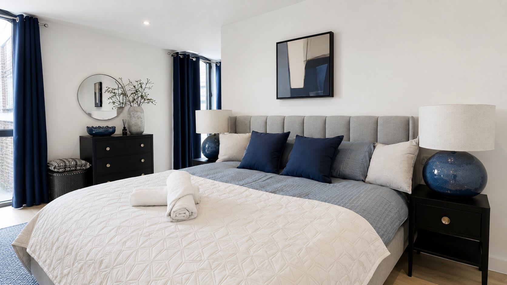 Une chambre à coucher moderne avec un grand lit, une table de chevet avec une lampe, une commode et un miroir au mur.