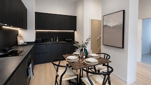 A modern kitchen with dark cabinetry, a dining area with a wooden table set for four, and a minimalist painting on the wall. - Downtown Manchester Townhouse w/ Garden & Modern (Greater Manchester)
