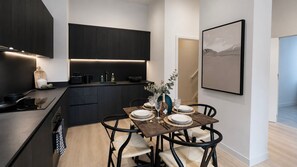 Una cocina moderna con armarios oscuros, un comedor con mesa de madera dispuesta para cuatro personas y un cuadro minimalista en la pared.