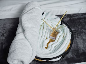 A bottle of French vanilla candle with a label, surrounded by rolled towels on a tray.